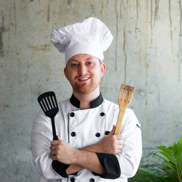 Confident professional chef in uniform arms crossed and holding spatula in his hands Confident professional chef in uniform arms crossed and holding spatula in his hands. indoors restaurant hotel work tool stock pictures, royalty-free photos & images