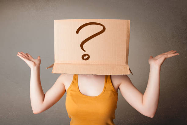 istock Young lady gesturing with a cardboard box on her head with question mark 948504134