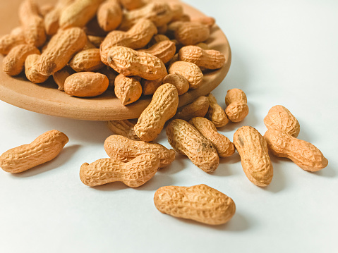 Close-up of groundnuts in a terracotta container placed on a white background.