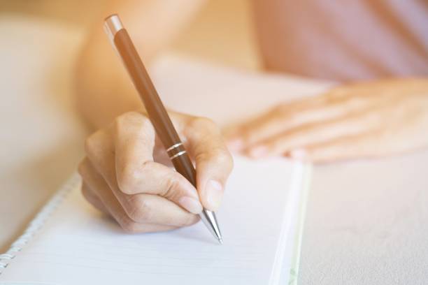 istock close up hand woman are writing notepad down cost into the book sit on the sofa. 948507348