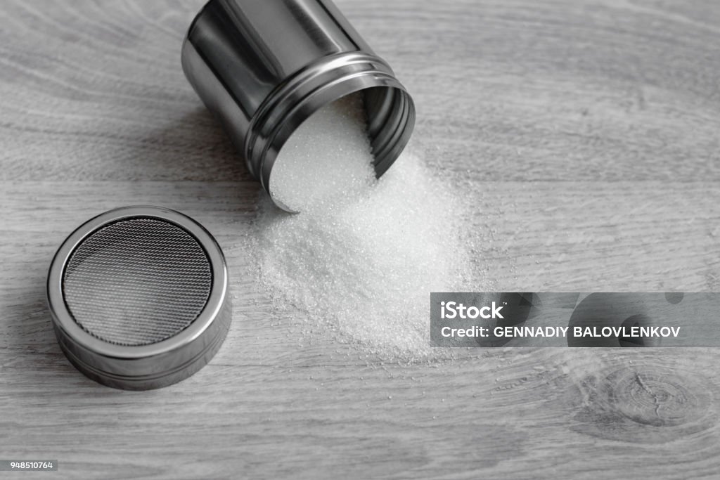 Sweet cooking, white sugar and a metal container with a lid in a mesh on a wooden background Sweet cooking, white sugar and a metal container with a lid in a mesh on a wooden background. Above Stock Photo