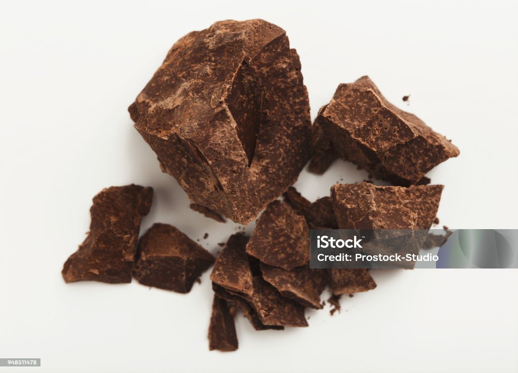 Heap of chocolate pieces isolated on white Pieces of dark chocolate isolated on white background. Heap of broken block chocolate, cutout Addiction Stock Photo