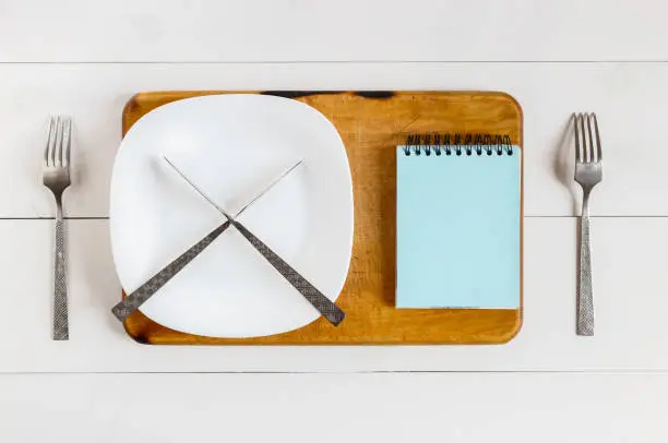Concept - stop eating. On an empty plate, knive a cross lie. Nearby mock up clean sheet of paper. Template. On a chopping kitchen board. Top view