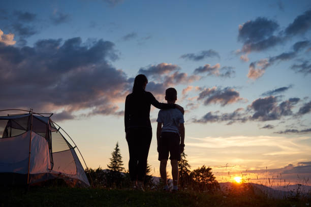 Photo of Rear view of mother hugs her son near tent on top of mountain enjoying view of sun