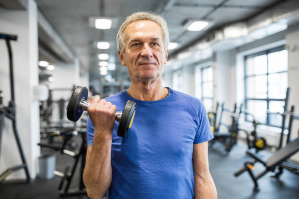 Strong senior man holding dumbbell in gym Portrait of strong senior man holding dumbbell in gym senior bodybuilders stock pictures, royalty-free photos & images