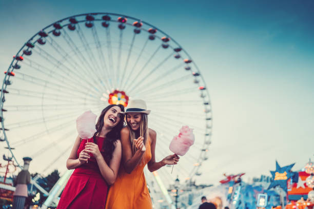Happy women at the amusement park Two friends eating cotton candy and laughing at the amusement park ferris wheel stock pictures, royalty-free photos & images