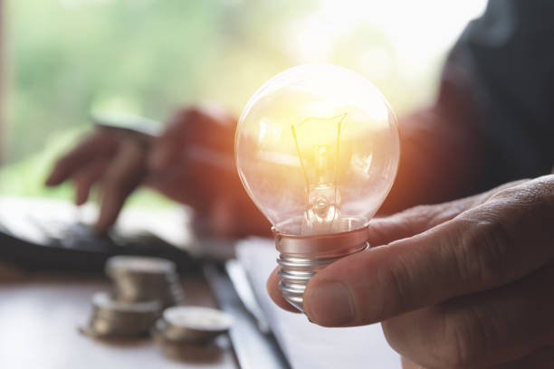 istock Hand holding light bulbs glowing and using calculator. Idea, creativity and saving energy with light bulbs concept. 948556294