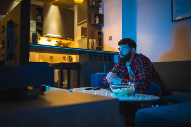 istock Young bearded men watching sport on television with his dog 948556510