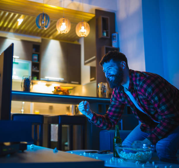 istock Young bearded men watching sport on television with his dog 948556514