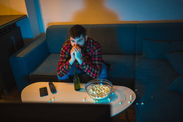 istock Young bearded men watching sport on television with his dog 948556544