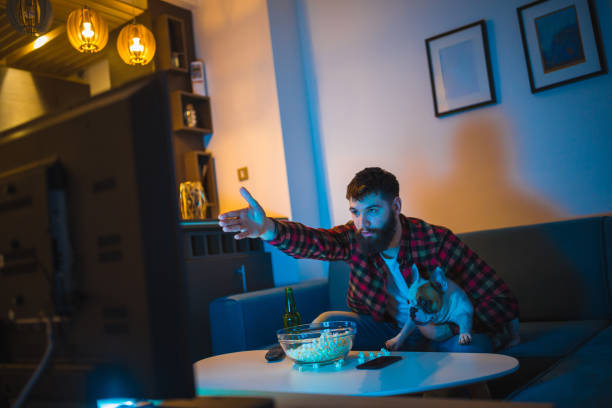 Young bearded men watching sport on television with his dog