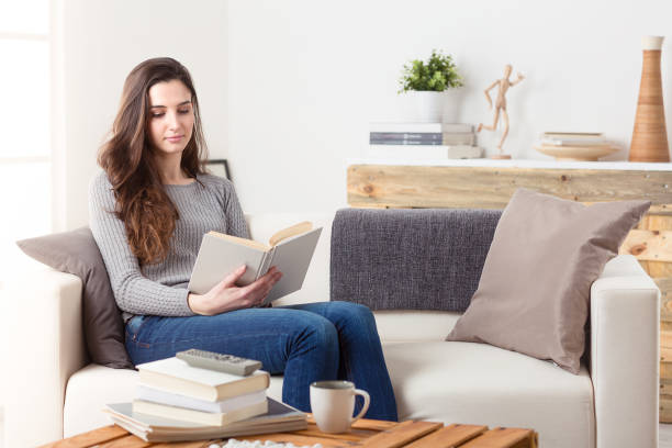 istock Woman reading a book sitting on a couch at home 948559310