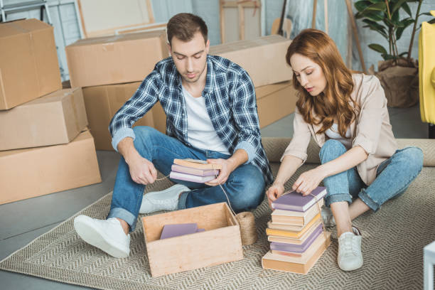 istock young couple sitting on carpet and packing books in box during relocation 948575974