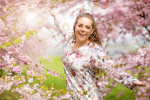 Beautiful Blonde Woman alone in Cherry Blossom Forest embracing nature with open arms