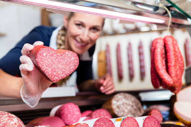 ventas mujer en tienda de carne mostrando una salchicha en forma de corazón - sausage shaped fotografías e imágenes de stock