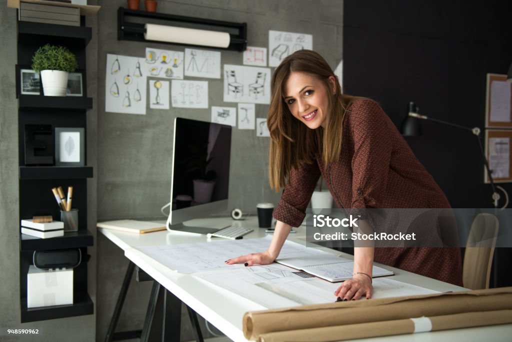 Smiling designer in her studio Young smiling female designer standing in front of her designs Entrepreneur Stock Photo