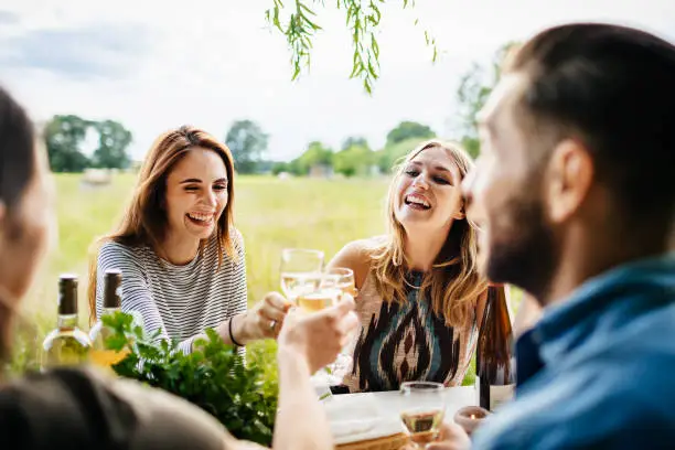A young group of friends smiling and drinking wine together while having lunch at a local farm.