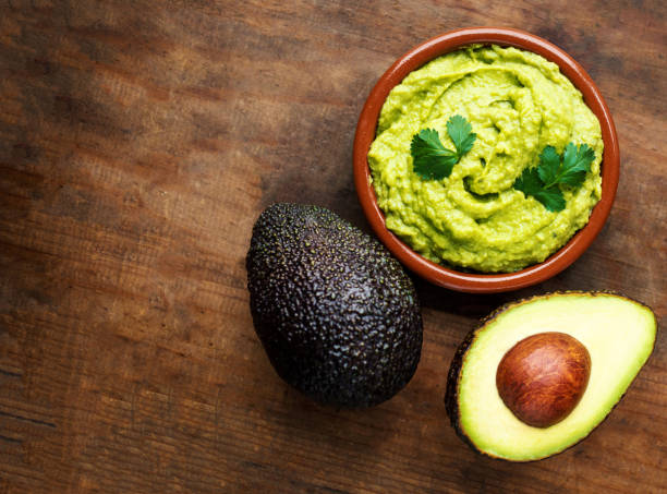 Avocado with guacamole sauce on a dark wood background. Half and whole avocadoes close up. Top view. Copy space"n Avocado with guacamole sauce on a dark wood background. Half and whole avocadoes close up. Top view. Copy space"n guacamole photos stock pictures, royalty-free photos & images