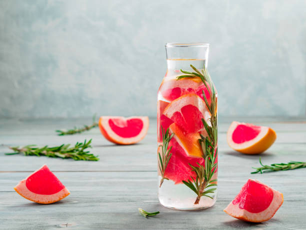 infused detox water with grapefruit and rosemary infused detox water with grapefruit and rosemary in glass bottle on gray wooden table. diet healthy eating and weight loss concept, copy space for text infused water stock pictures, royalty-free photos & images