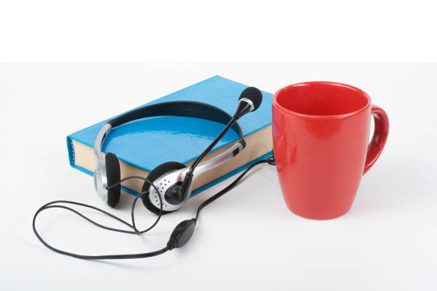 istock Audiobook on white background. Headphones put over blue hardback book, empty cover, red cup, copy space for ad text. Distance education, e-learning concept 948600968