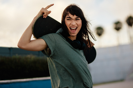 Portrait of excited woman skateboarder outdoors at skate park.  Woman with her skate board looking at camera and laughing outdoors.
