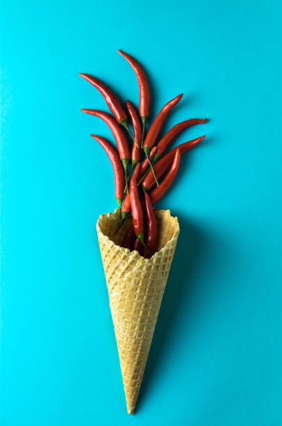 istock Ice cream waffle cone with red hot little chili peppers on the blue background. 948601832
