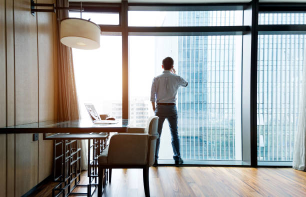 istock Businessman standing by the window using phone 948606122