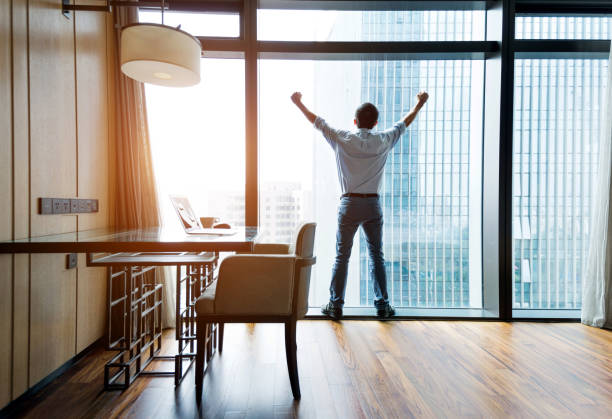 istock Businessman standing by the window with arms raised 948606328