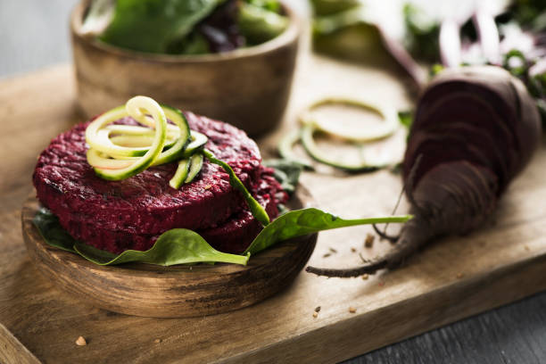 beet burgers on a wooden table closeup of some beet burgers on a wooden chopping board placed on a rustic wooden table, next to a sliced beet spanish hamburger stock pictures, royalty-free photos & images