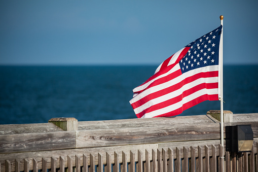 Small American flag on a flagpole blowing in the wind at the beach on a pier in Charleston, South Carolina