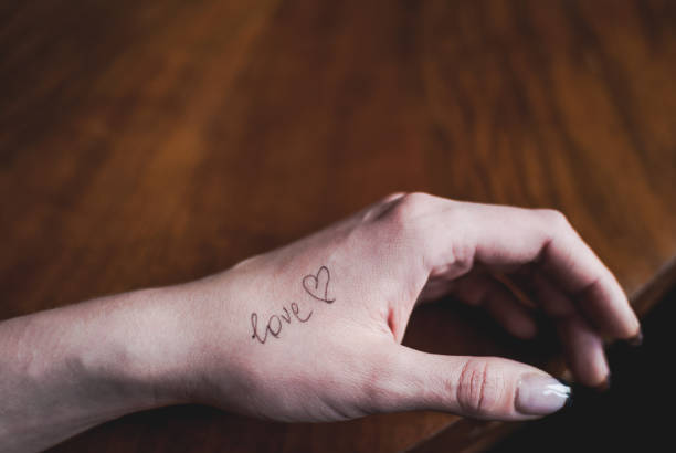 Close-up of girl's tender pale hand with word "love" Close-up of girl's tender pale hand with a word "love" and heart shape written on it the human body writing black human hand stock pictures, royalty-free photos & images