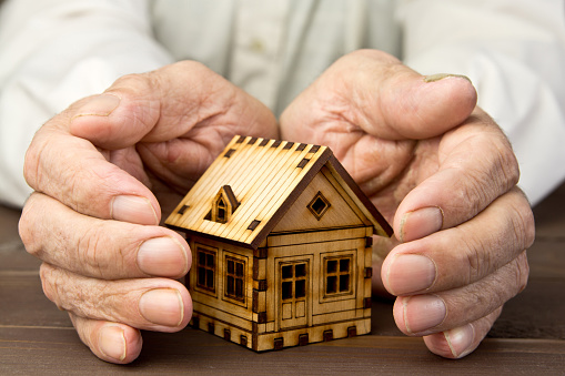 Old man protecting house model with hands .Risk insurance. The concept of mortgages and Bank loans. Poverty. Rental property.
