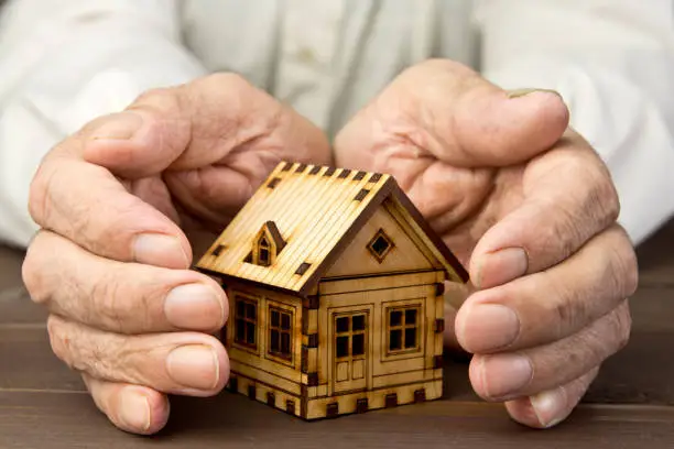 Photo of Old man protecting house model with hands .Risk insurance. The concept of mortgages and Bank loans. Poverty. Rental property.