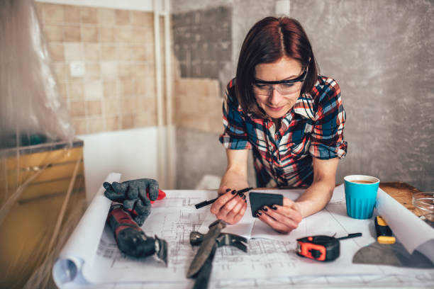 женщина с помощью смартфона во время ремонта кухни - home decorating interior designer blueprint planning стоковые фото и изображения
