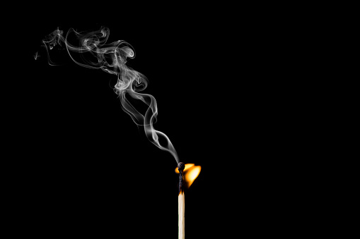 Matchstick burning with little flame and smoke on black background. Studio shoot image.
