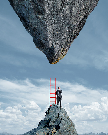 A businessman stands on top of a mountain peak holding a red ladder as he looks up at the impossible situation of having to climb to a much larger inverted mountain peak directly above him.
