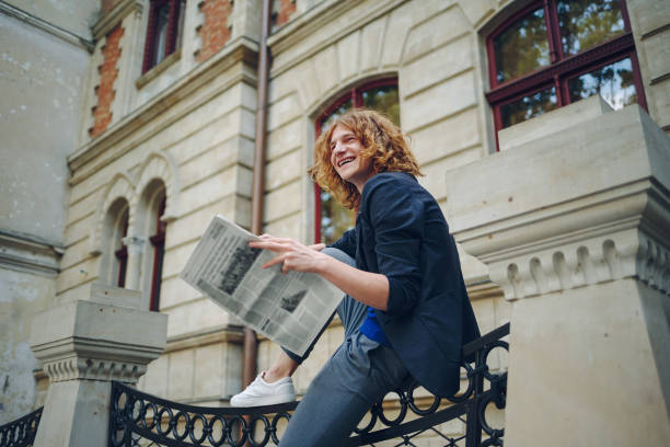 Young reddish man reading newspaper near old style building
