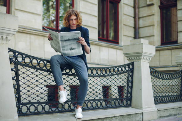 istock Attractive man reading newspaper near old style building 948675454