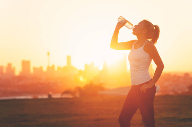 Silhouette of a woman drinking form a cold water bottle. Silhouette of a woman drinking form a cold water bottle. She is exercising at sunset or sunrise. City of Sydney in the background. Copy space. sports training australia stock pictures, royalty-free photos & images