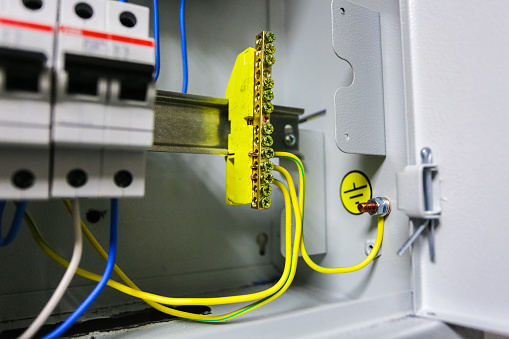Electrical yellow green ground wires is connected to ground copper bar or earth bonding bar in metal electric breaker box with electrical circuit breakers and electrical grounding sign near ground bolt inside box.