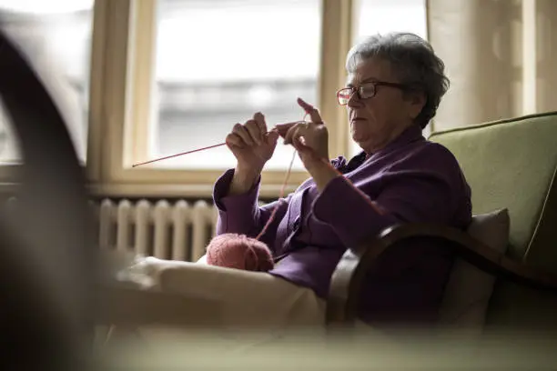 Senior women sitting at home and knitting near window