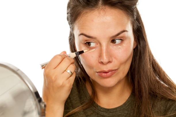 istock Young woman applying concealer under her eyes on white background 948752534