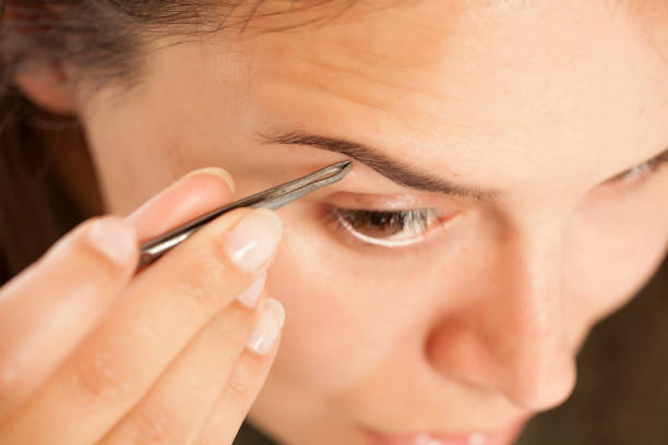 istock Young beautiful woman pluck her eyebrows with tweezers 948752536