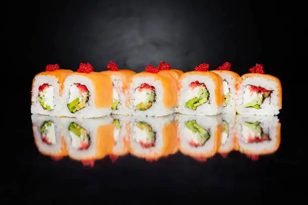 Roll Philadelphia on black background made of salmon, cucumber, nori, pickled rice, cheese, masago caviar, Sesame white. Traditional Japanese cuisine. Sushi menu. Japanese food. Free-space