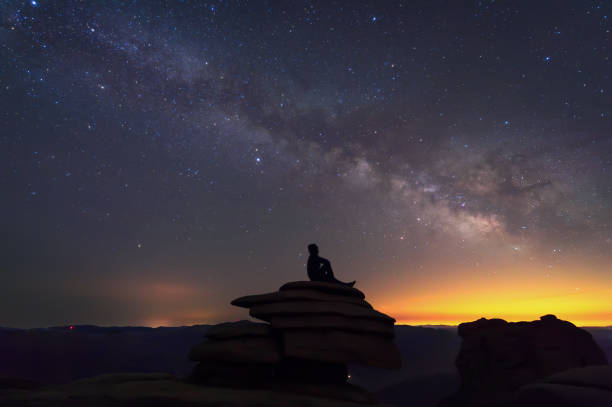 istock Man sitting on the rock under The Milky Way Galaxy 948764578