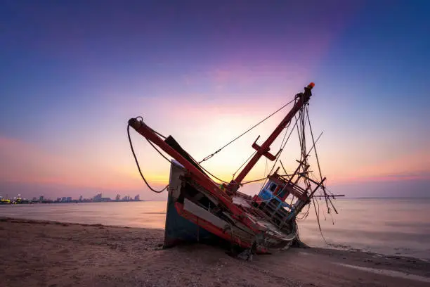 Abandoned shipwreck of wood fishing boat on beach at twilight time