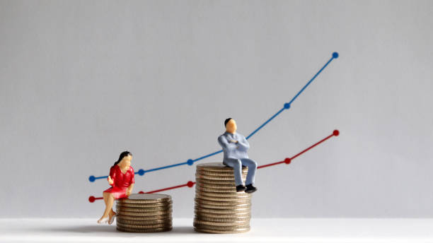 the concept of gender pay gap. a miniature man and a miniature woman sitting on top of a pile of coins at different heights in front of a bar graph. - uneven imagens e fotografias de stock