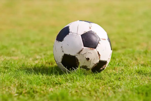 Photo of Old Soccer ball on a green grass. Football on a sports field. Sunny day. Sporting goods.