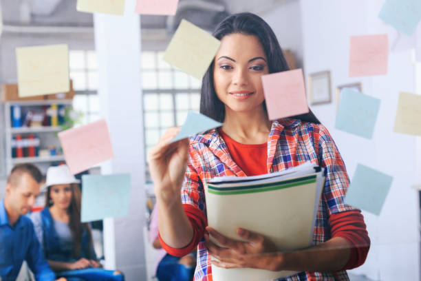 istock Smiling asian woman taking post-it notes from glass wall 948863722