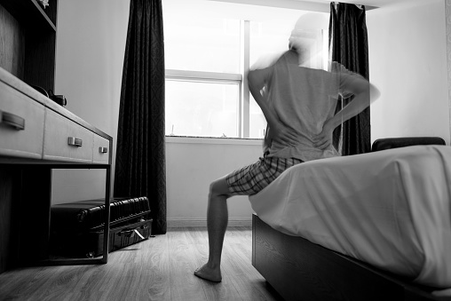 Man sitting on the edge of bed with backache